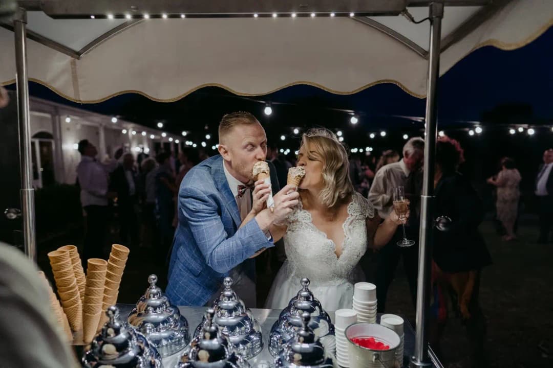 Couple enjoys ice cream together beside an outdoor dessert stand at night.