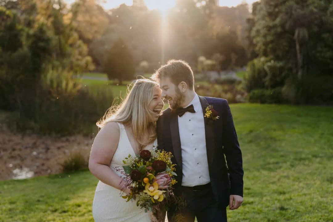 Couple embraces beside a pond with sunset light behind them.