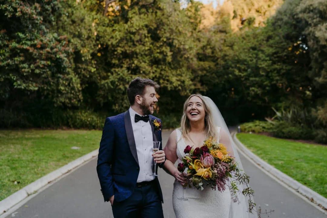 Couple laughs while walking along a quiet road holding a colourful bouquet.
