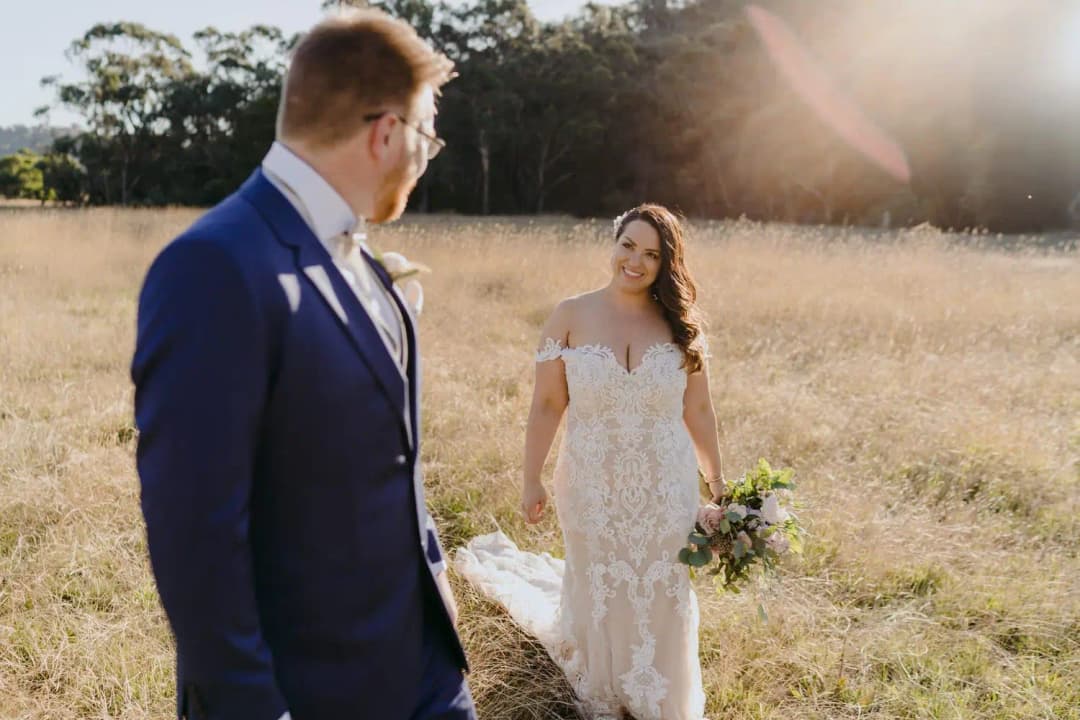 Groom turns toward the bride approaching through a sunlit dry field.