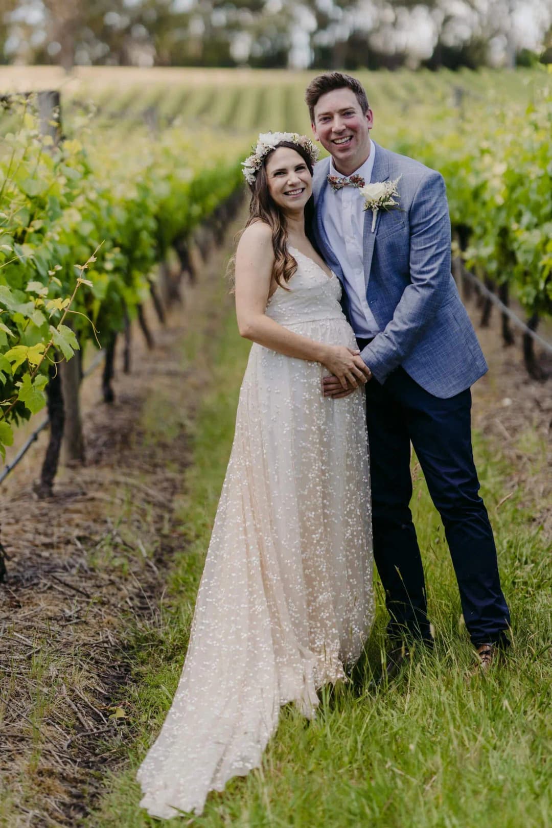 Couple poses together between green vineyard rows.