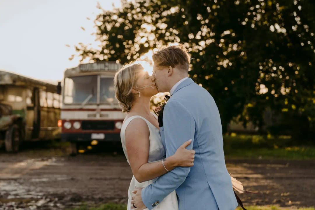 Couple kisses beside a caravan with low sunlight behind them.