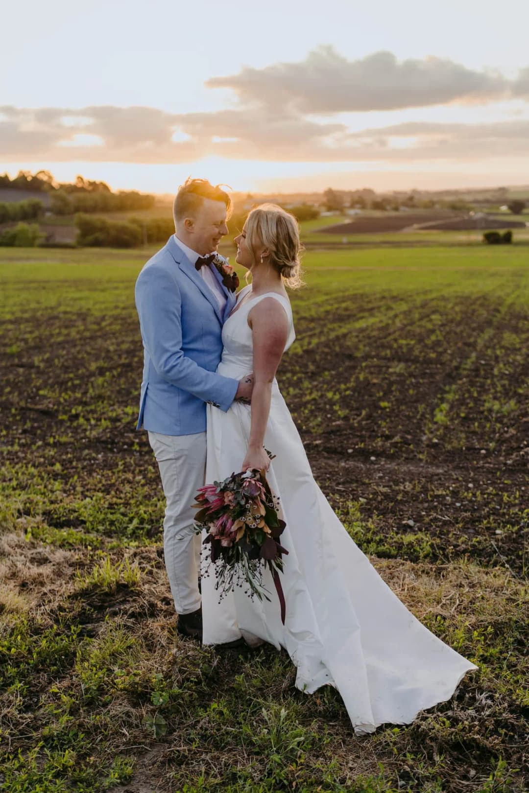 Couple kisses in a harvested field at sunset with the bride's train trailing behind her.