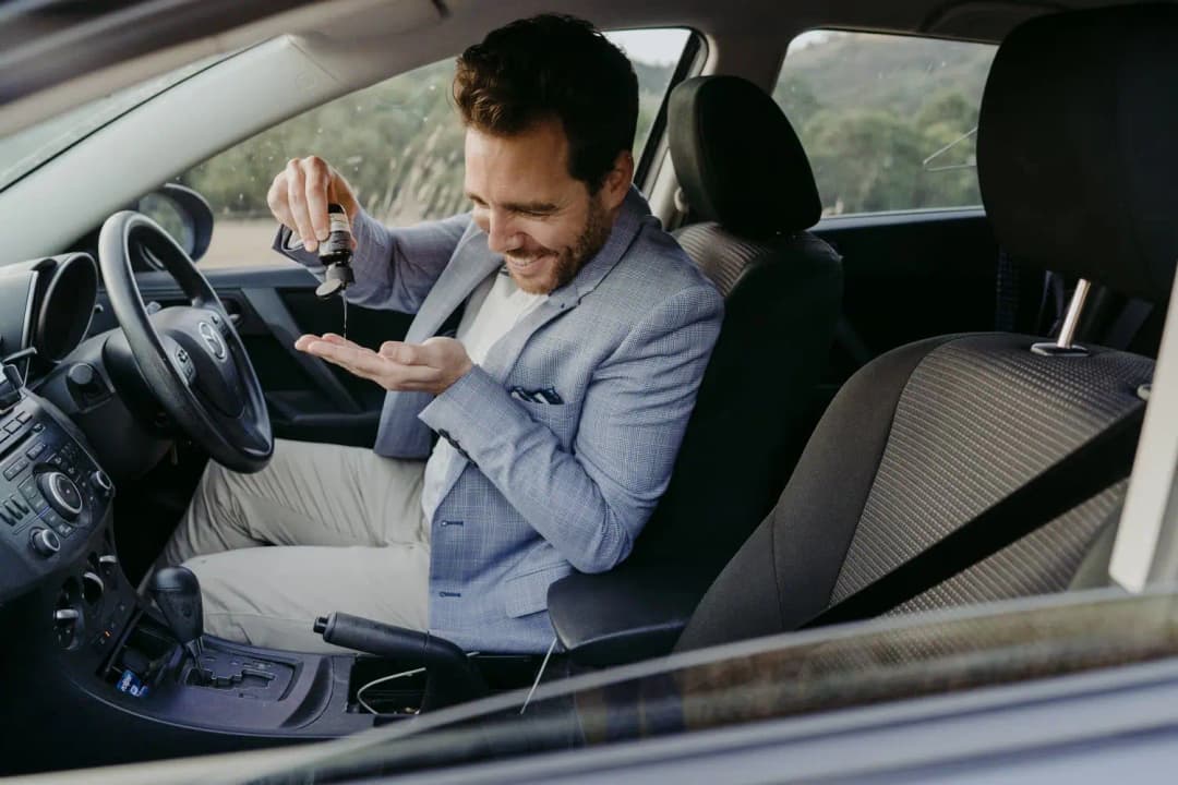 Groom pours a small drink into his hand while seated in a car.
