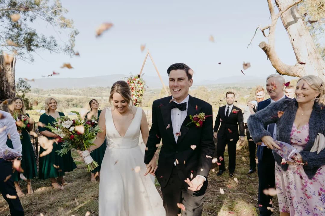 Newlyweds walk through guests tossing confetti at an outdoor ceremony.