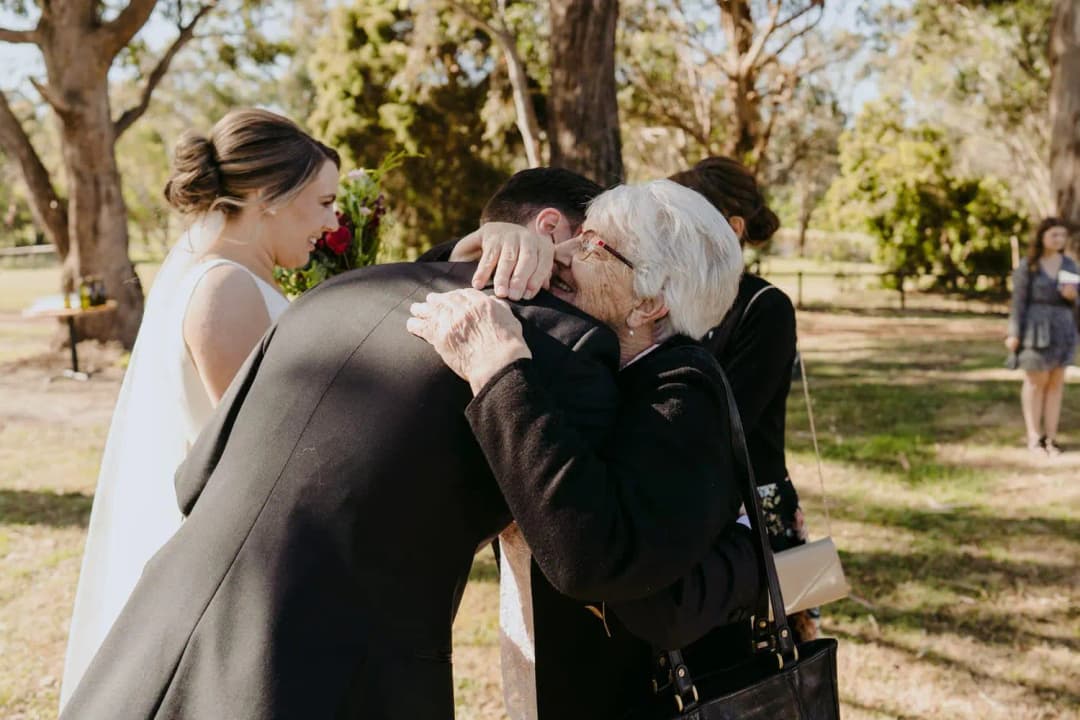 Older woman embraces the groom as the bride watches nearby.