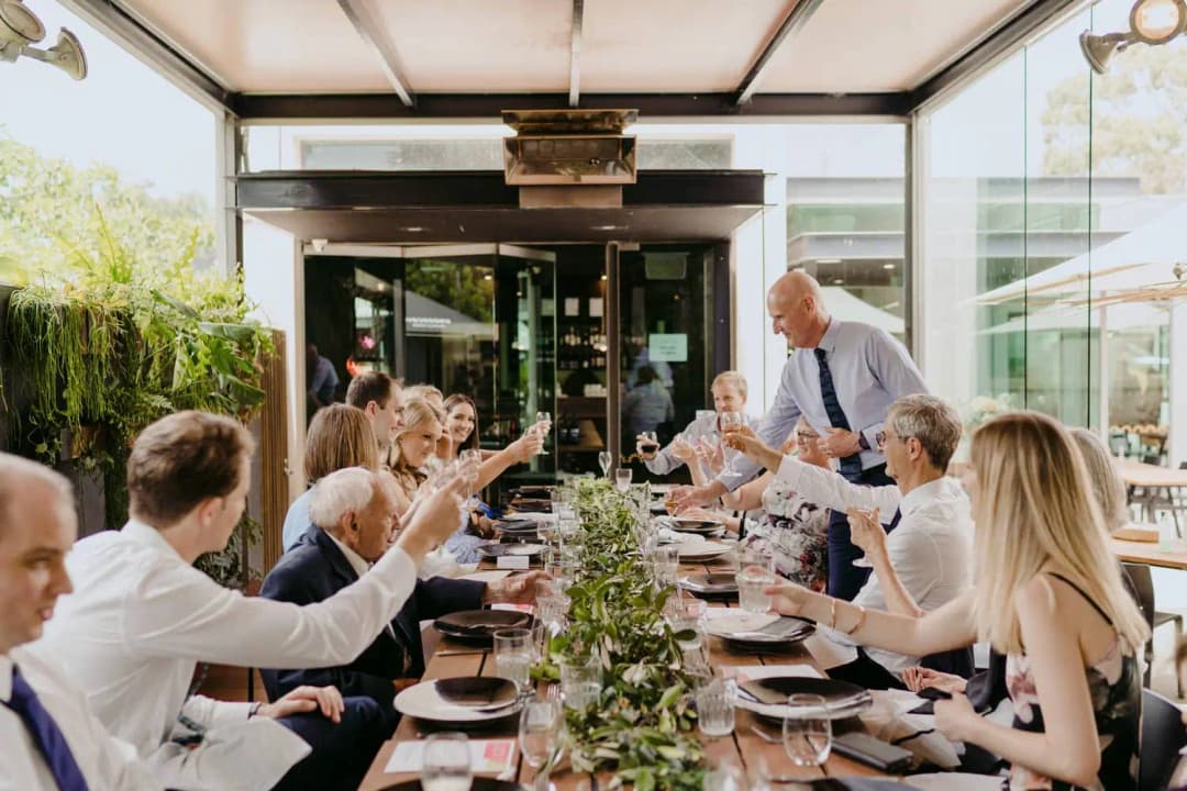 Guests raise glasses around a long outdoor reception table.