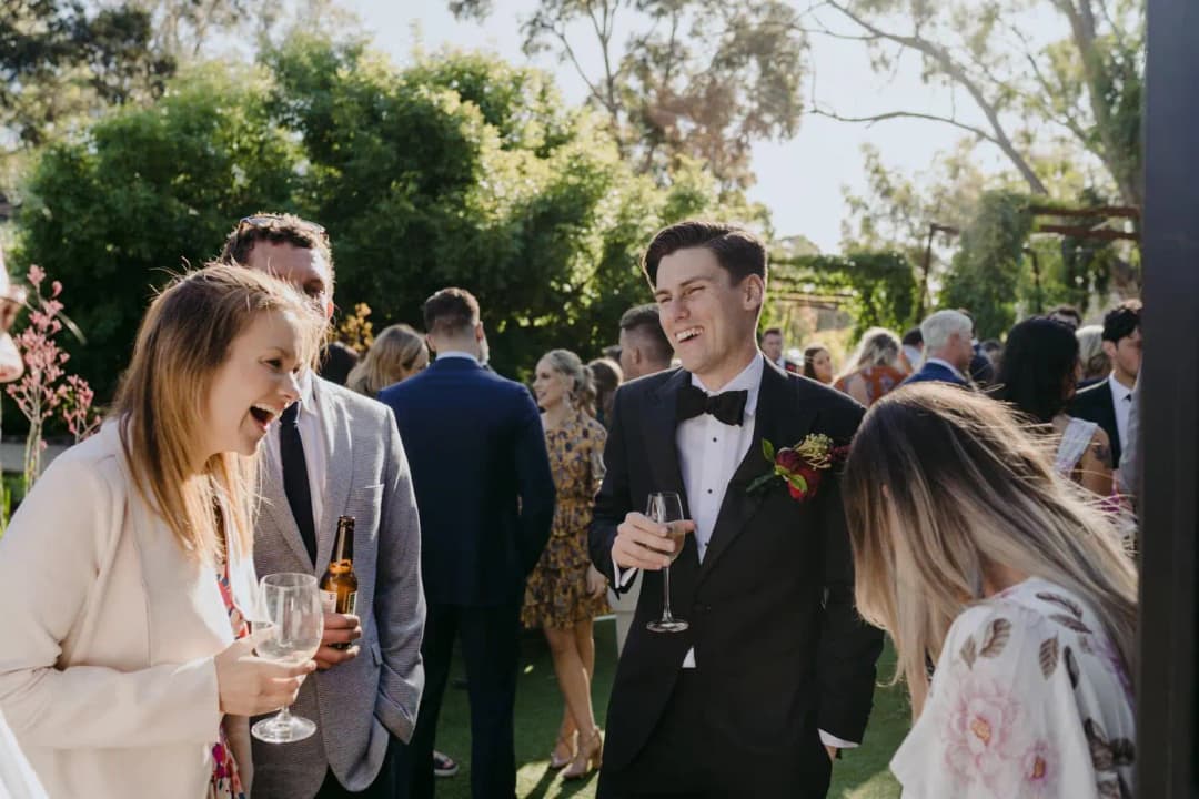 Guests laugh and chat over drinks in a sunlit garden.