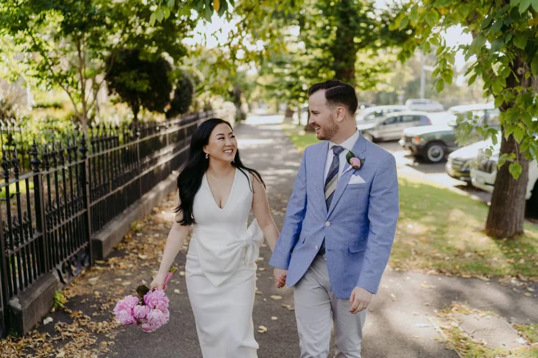 Couple walks hand in hand along a leafy residential street.