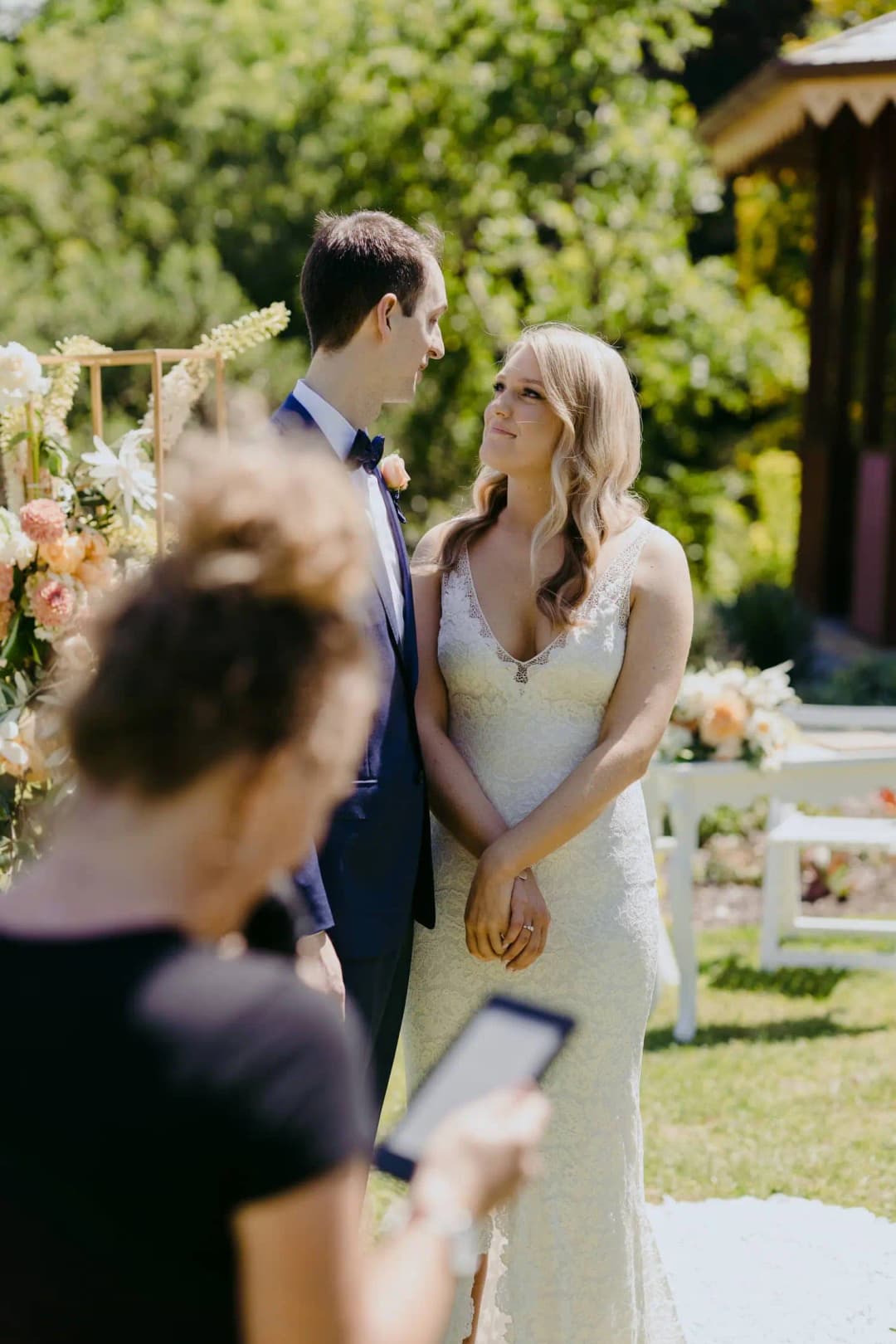 Couple smiles toward each other during a sunny garden ceremony.
