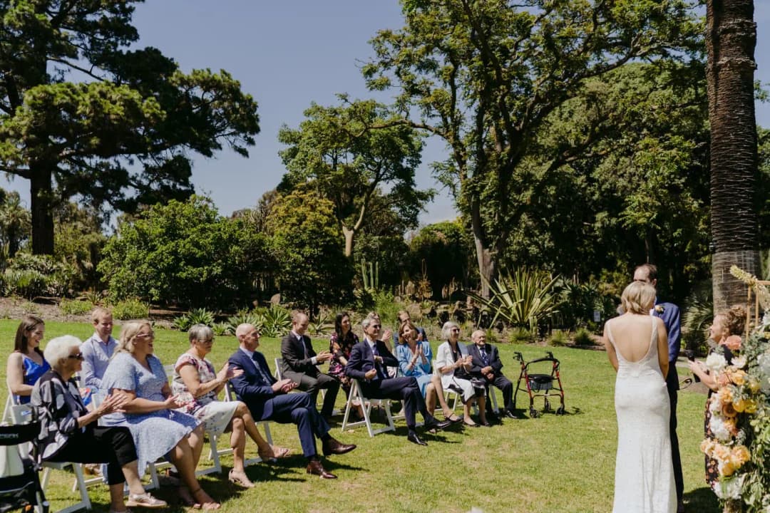 Seated guests watch the couple during a sunny garden ceremony.