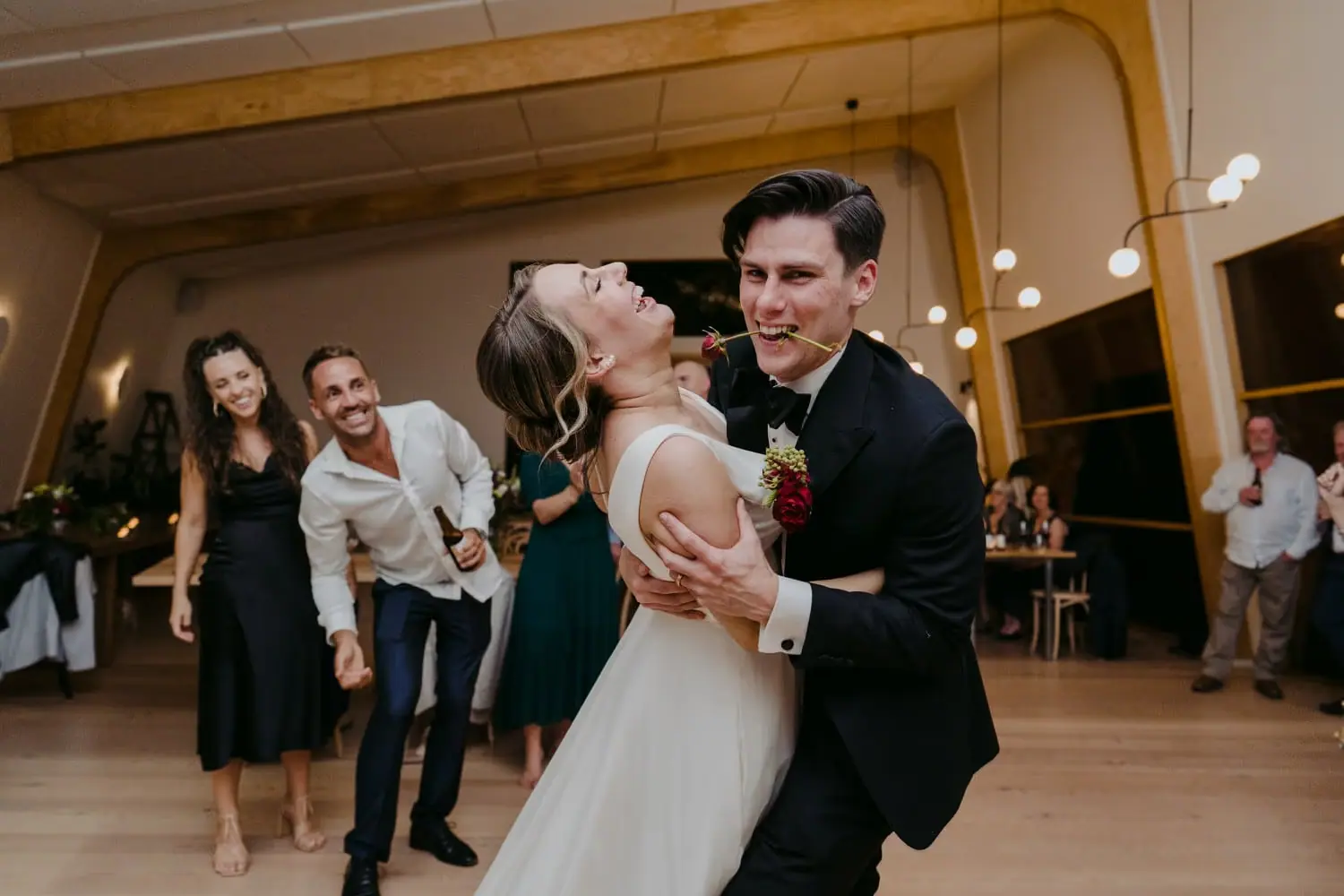 Groom dips the laughing bride on the dance floor while guests watch.