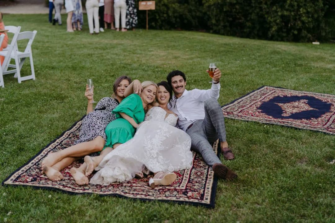Couple and two guests sitting together on patterned rugs on the grass.