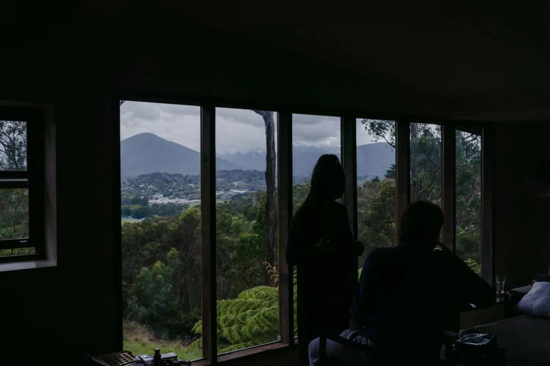 Silhouetted people beside wide windows overlooking green hills and distant mountains.
