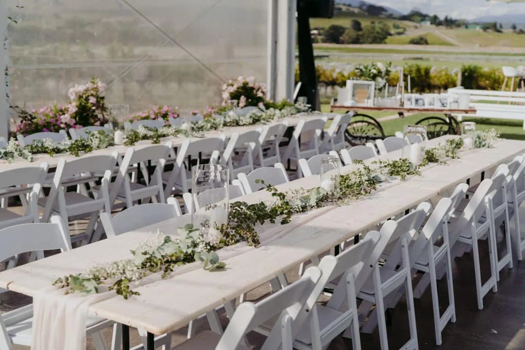 Long white reception tables decorated with greenery and pale flowers.