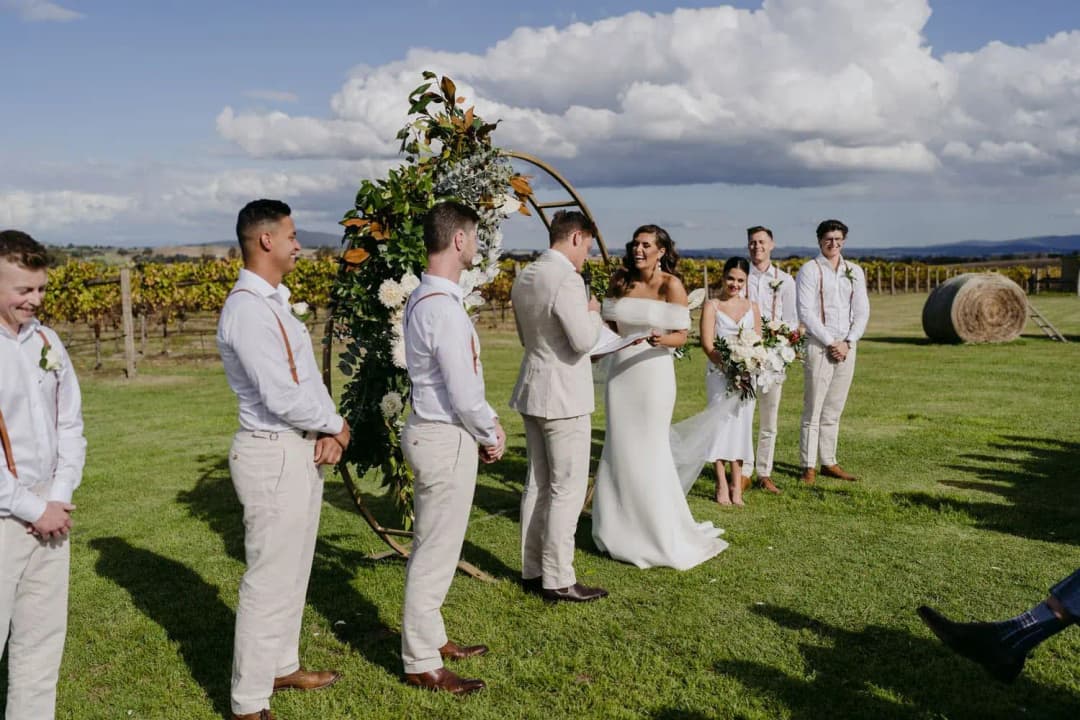 Wedding party standing beside the circular floral arch on the vineyard lawn.