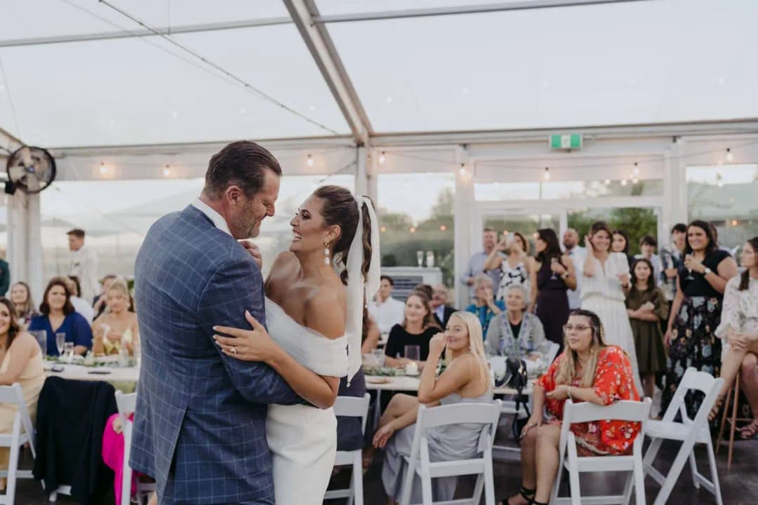 Bride dancing with a man in a blue suit while seated guests watch.