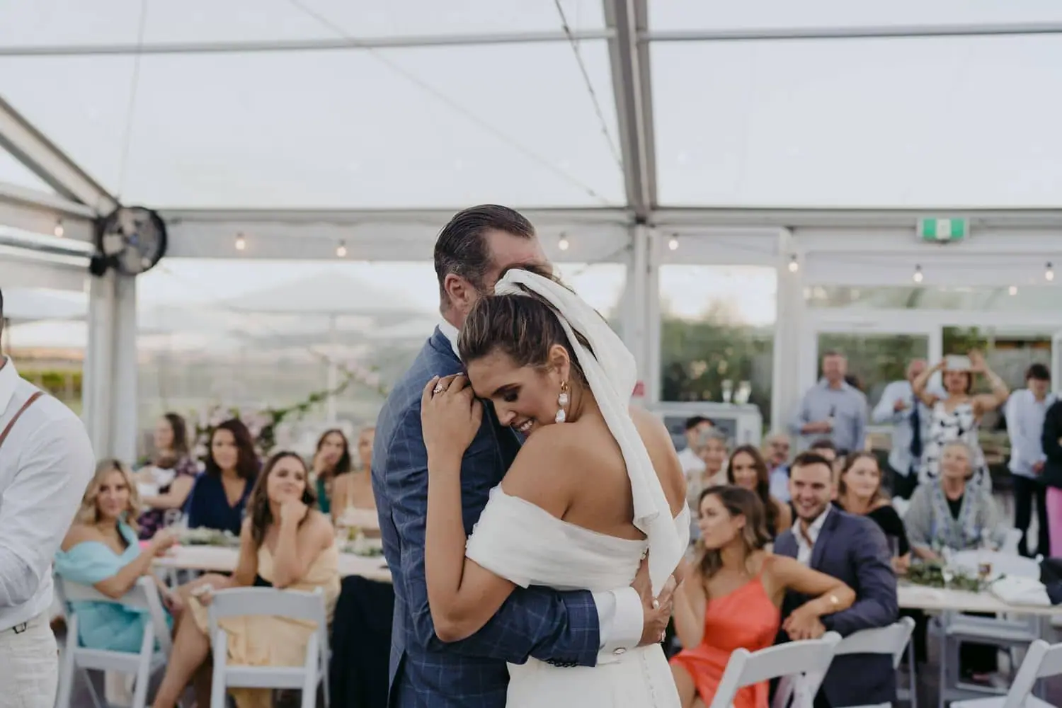 Bride embracing a man in a blue suit during a dance in front of their guests.