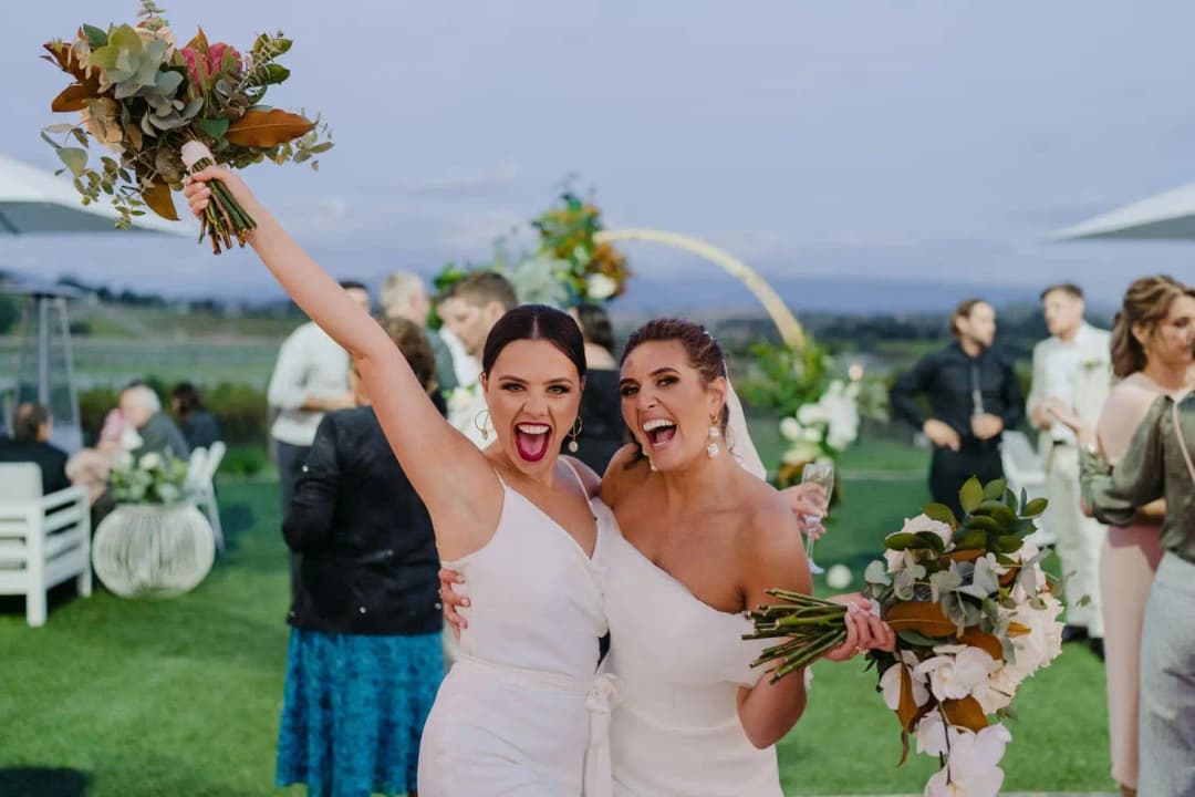 Bride and another woman smiling together while the woman raises a bouquet overhead.