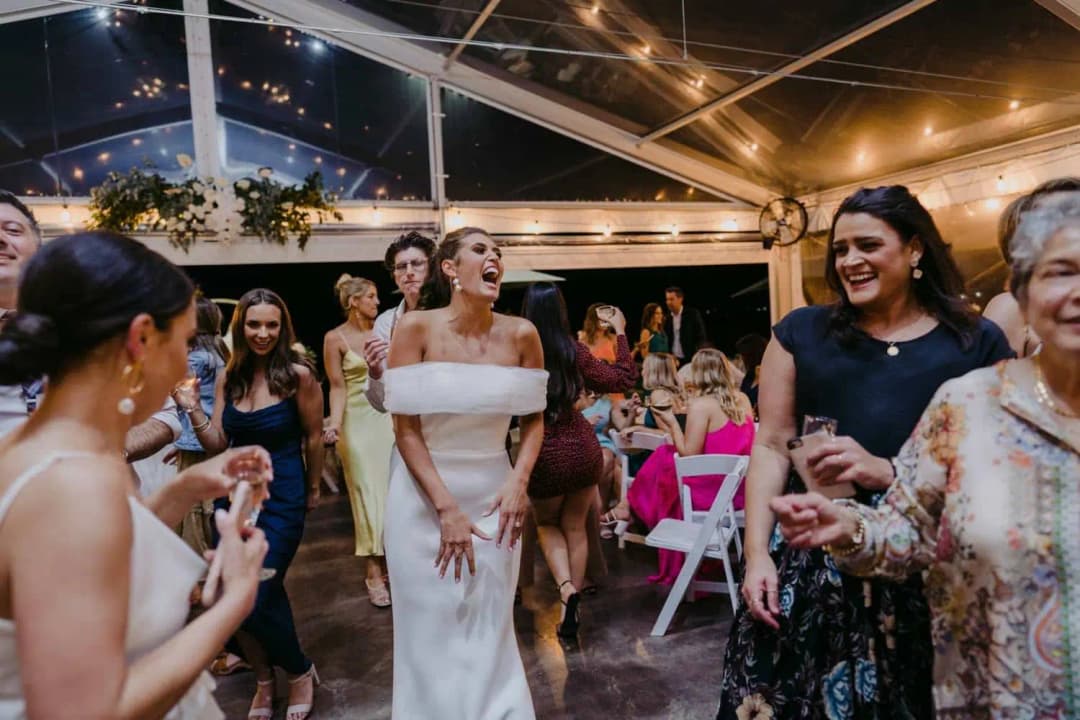 Bride laughing with guests on the dance floor under strings of lights.