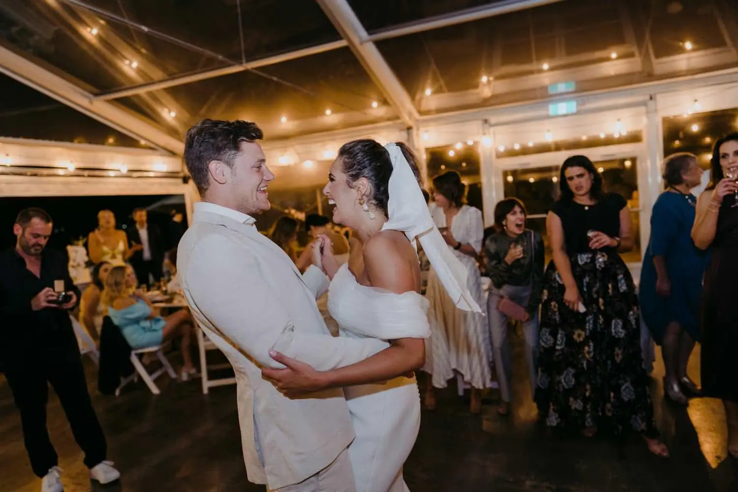 Bride and groom dancing together as guests watch inside the marquee at night.