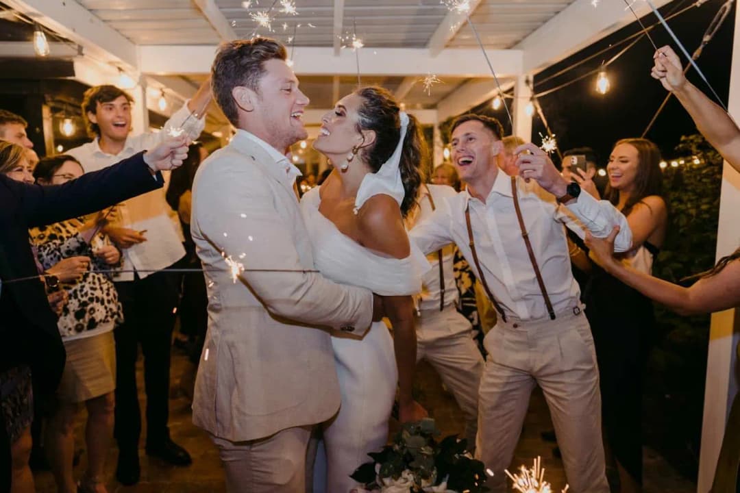 Bride and groom embracing while guests hold sparklers around them.
