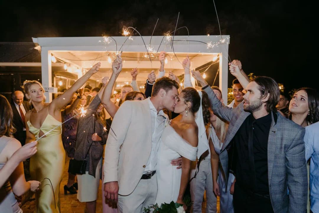 Couple kissing outside the marquee beneath sparklers held by their guests.