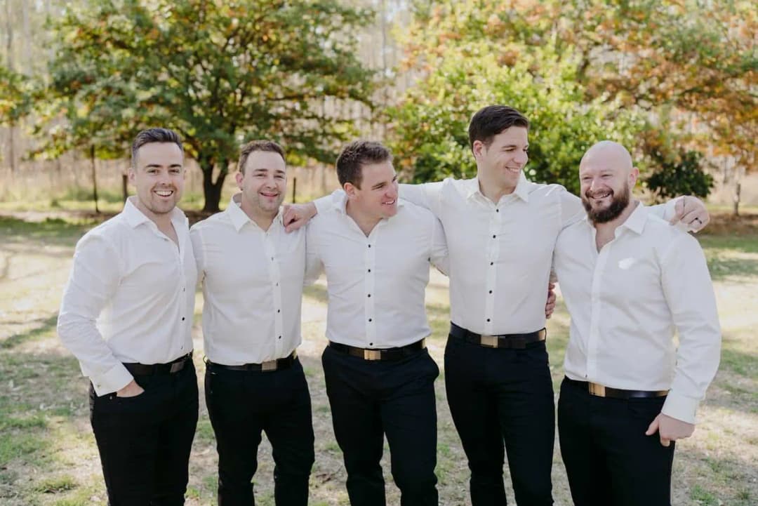 Five men in white shirts posing together on a garden lawn.
