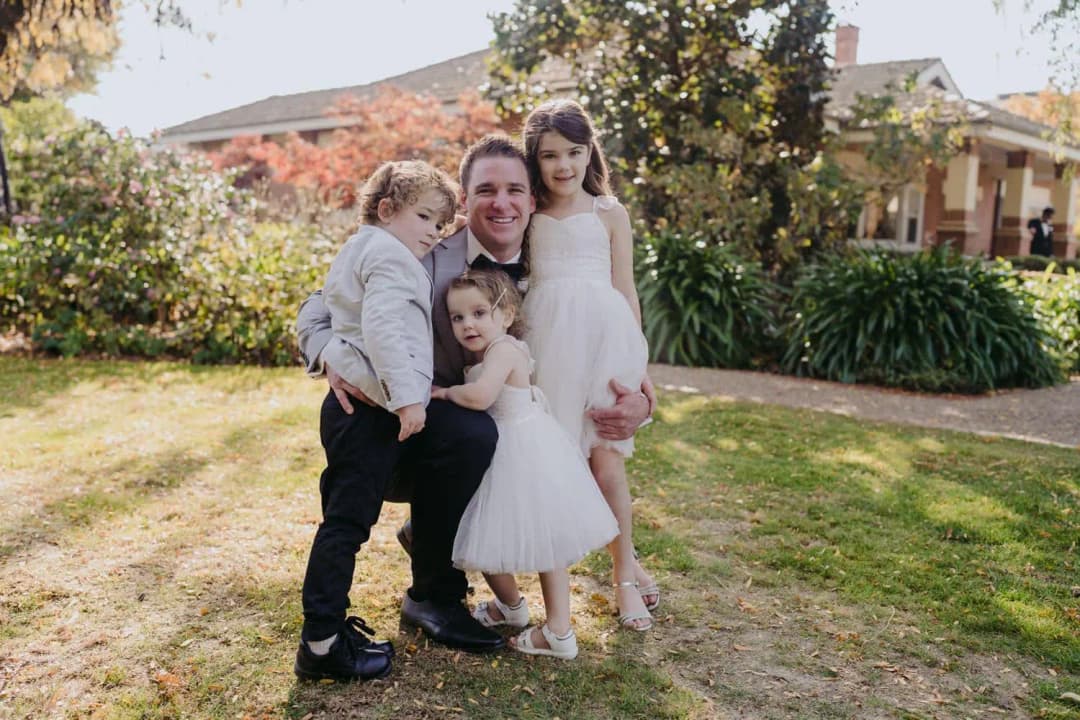 Groom posing with three children outside a brick house.