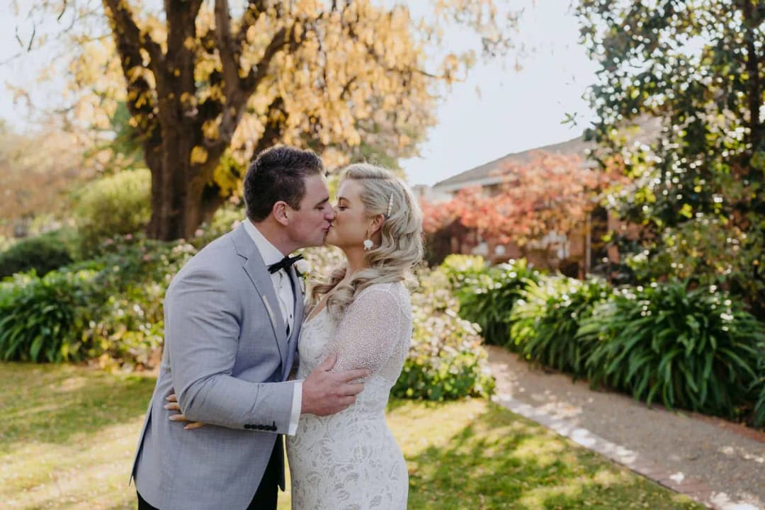 Bride and groom kissing beneath yellow autumn leaves.