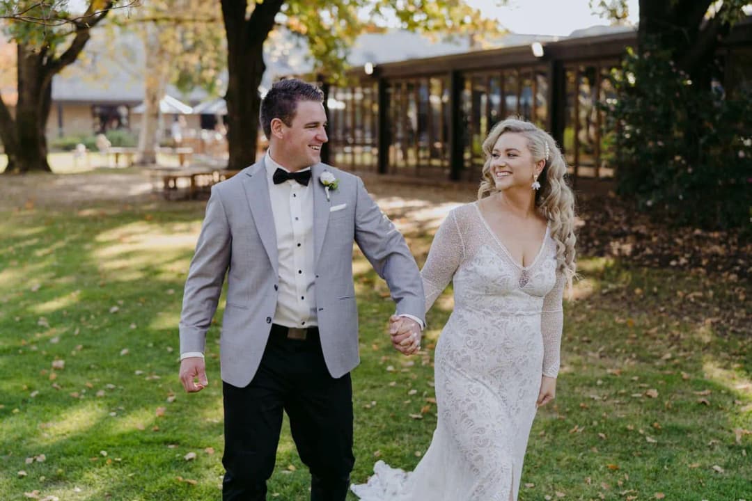 Bride and groom smiling and holding hands while walking through a garden.