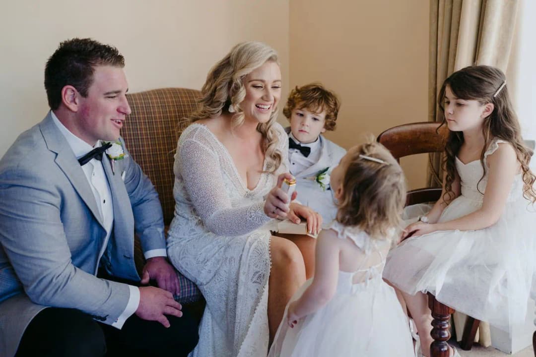 Bride and groom talking with three children gathered around them indoors.