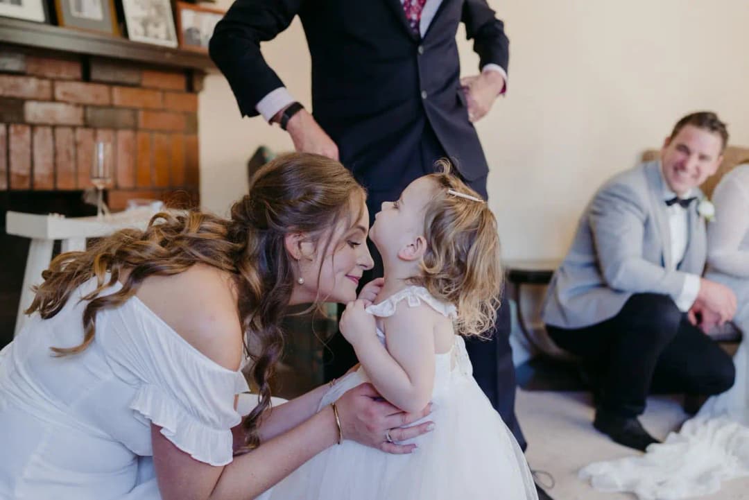 Woman leaning close to a smiling little girl while the groom watches.