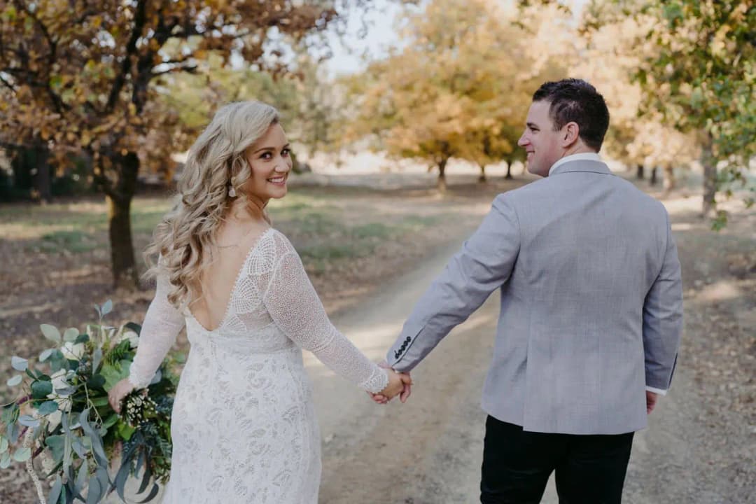 Bride looking back while holding the groom's hand on an autumn garden path.