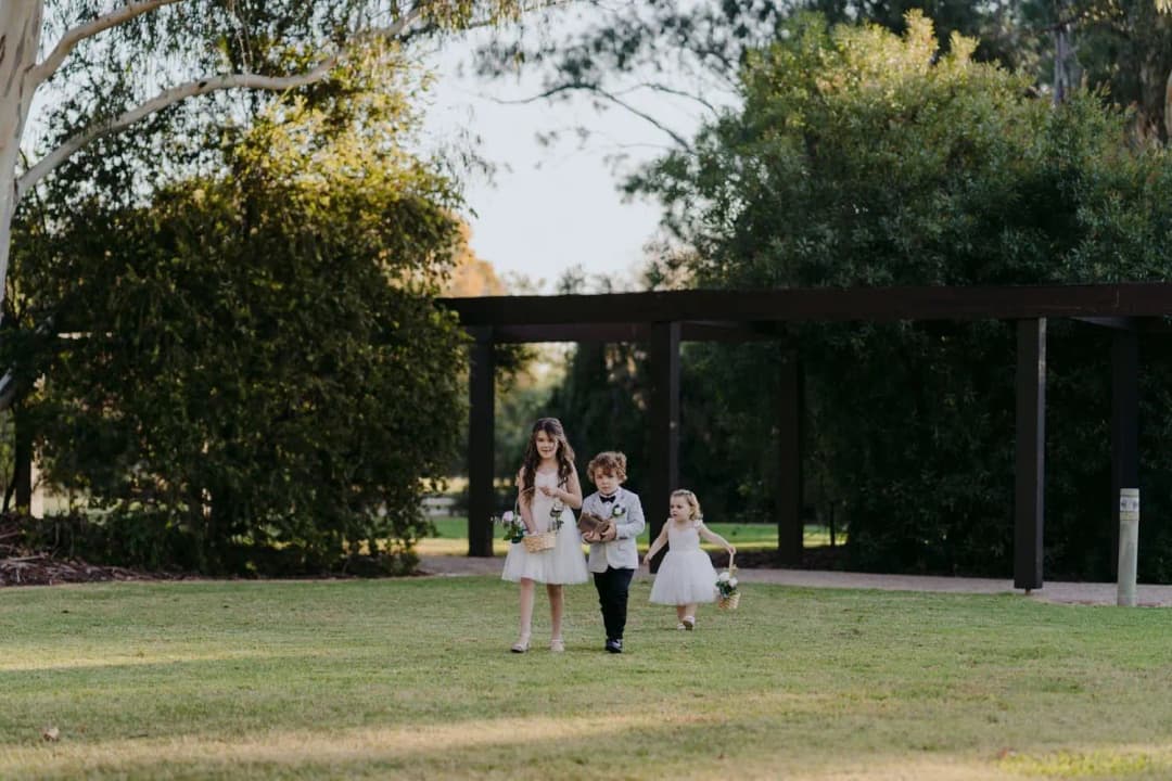 Three children walking across the lawn toward the outdoor ceremony.