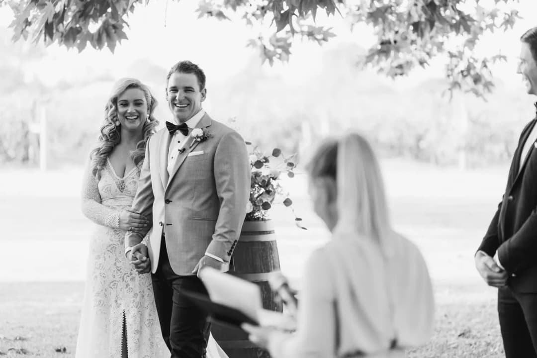 Black-and-white photograph of the smiling couple listening to the celebrant.