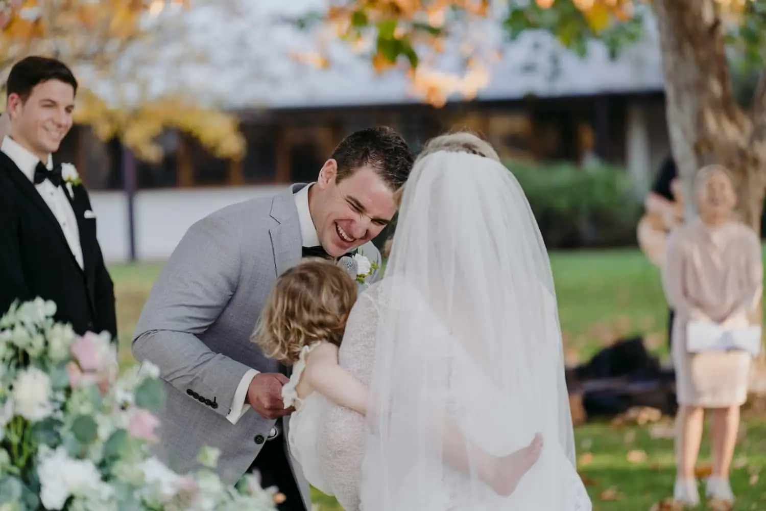 Groom bending down toward a small child beside the bride during the ceremony.