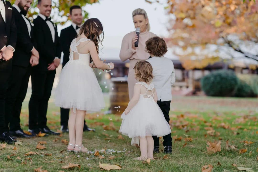 Three children standing beside the celebrant as she speaks into a microphone.
