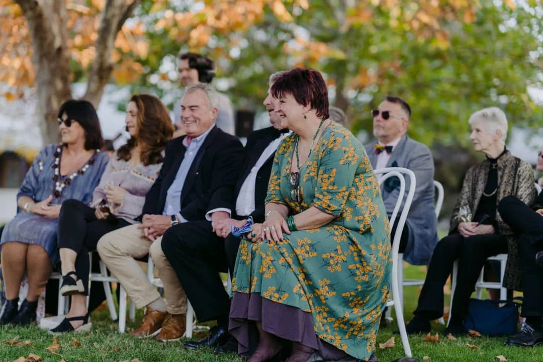 Seated guests smiling beneath autumn trees at the ceremony.