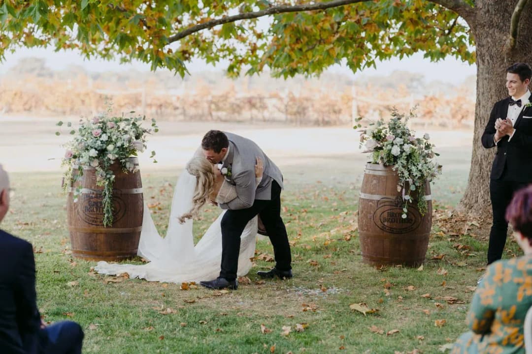 Groom dipping and kissing the bride beneath the ceremony tree.