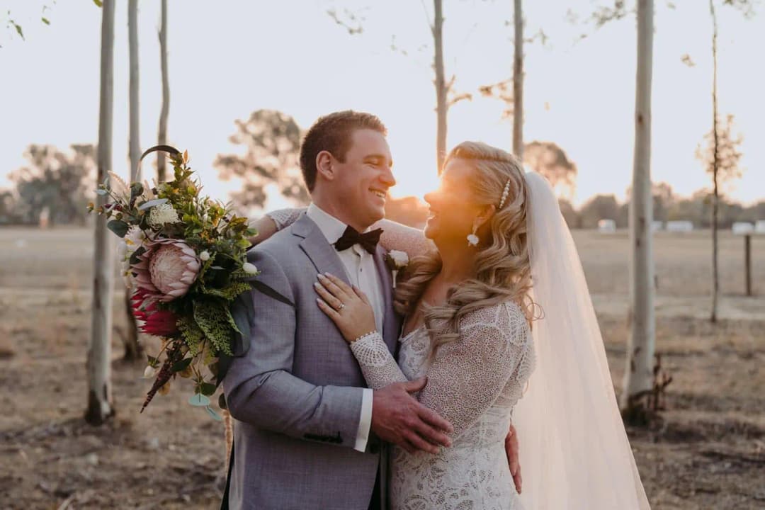 Couple embracing among slender trees with the setting sun behind them.