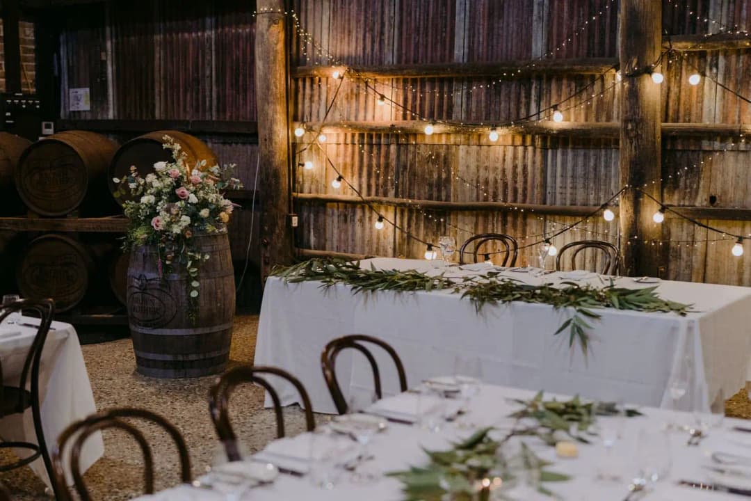 Flower arrangement on a barrel beside a white reception table in a rustic shed.