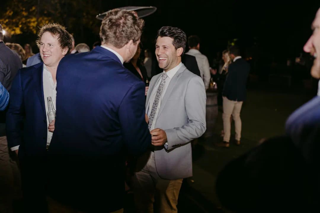 Groom laughing with guests outside the reception at night.