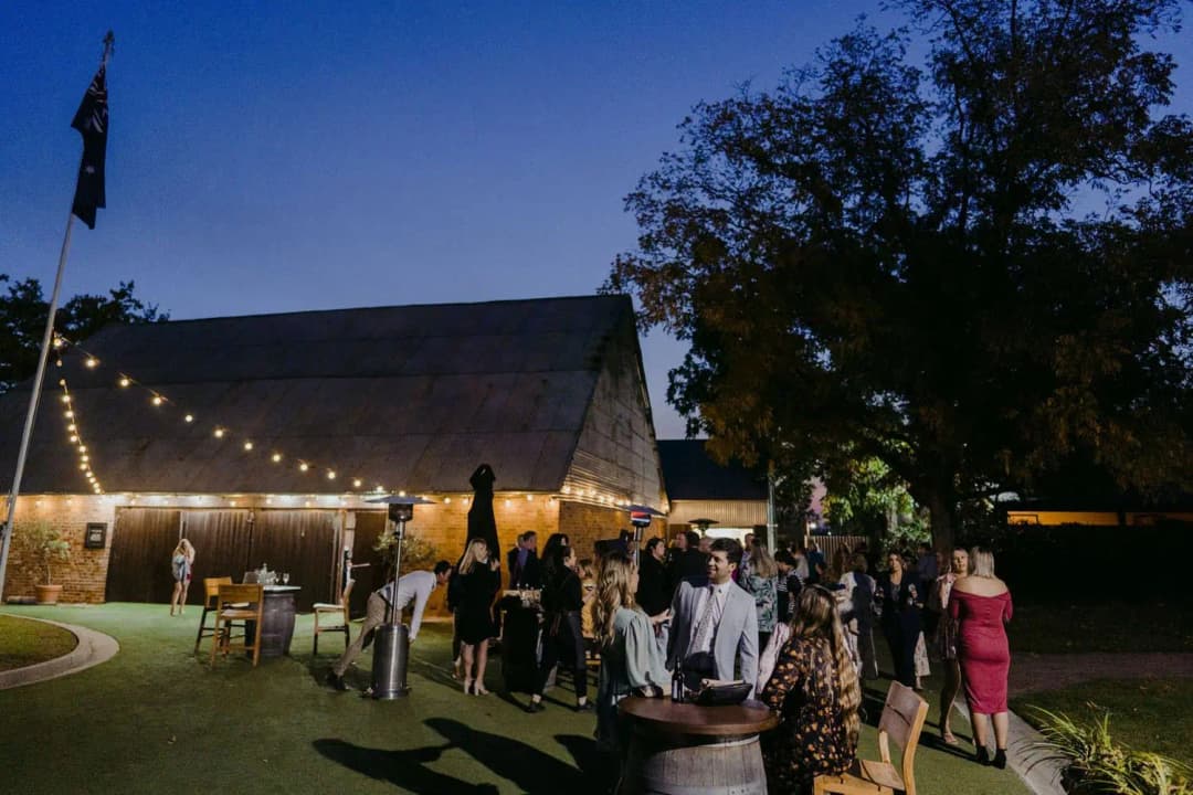 Guests socialising on the lawn outside the illuminated reception building at dusk.