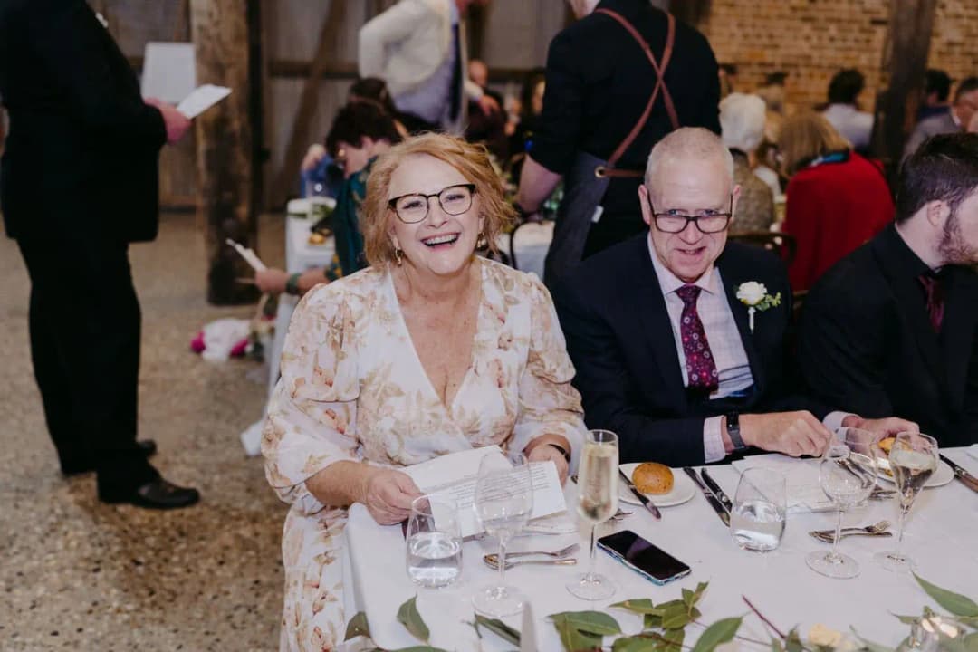 Woman and man in glasses smiling together at a reception table.