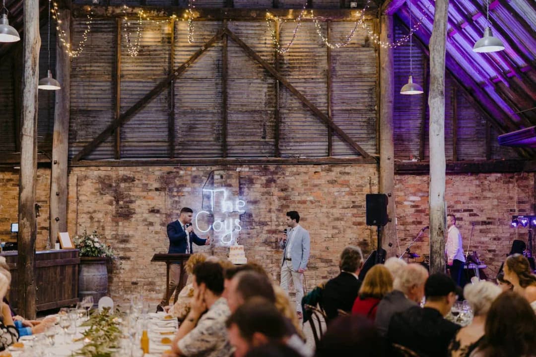 Guests watching speakers at the front of a rustic reception room.