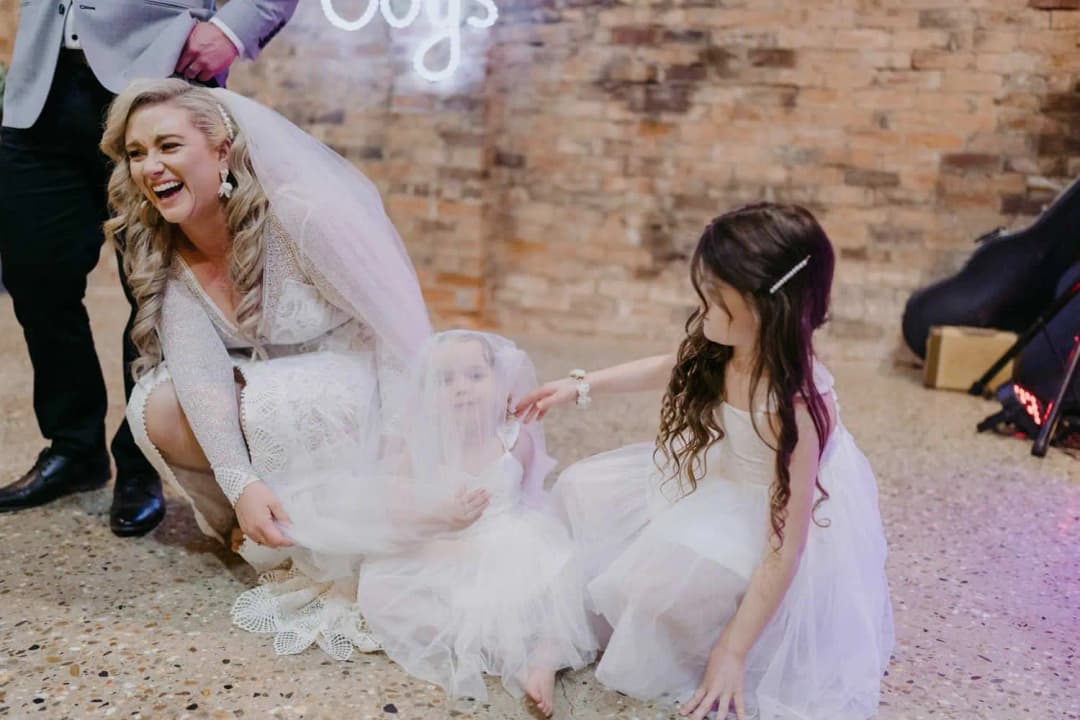 Bride laughing with two young girls beside the wedding cake table.