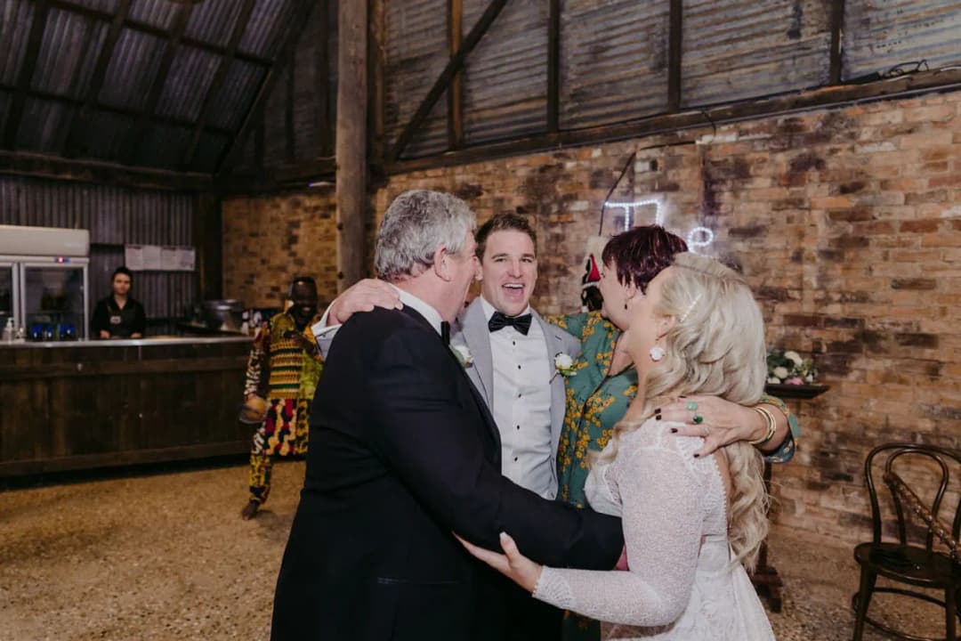Bride and groom embracing two guests on the dance floor.