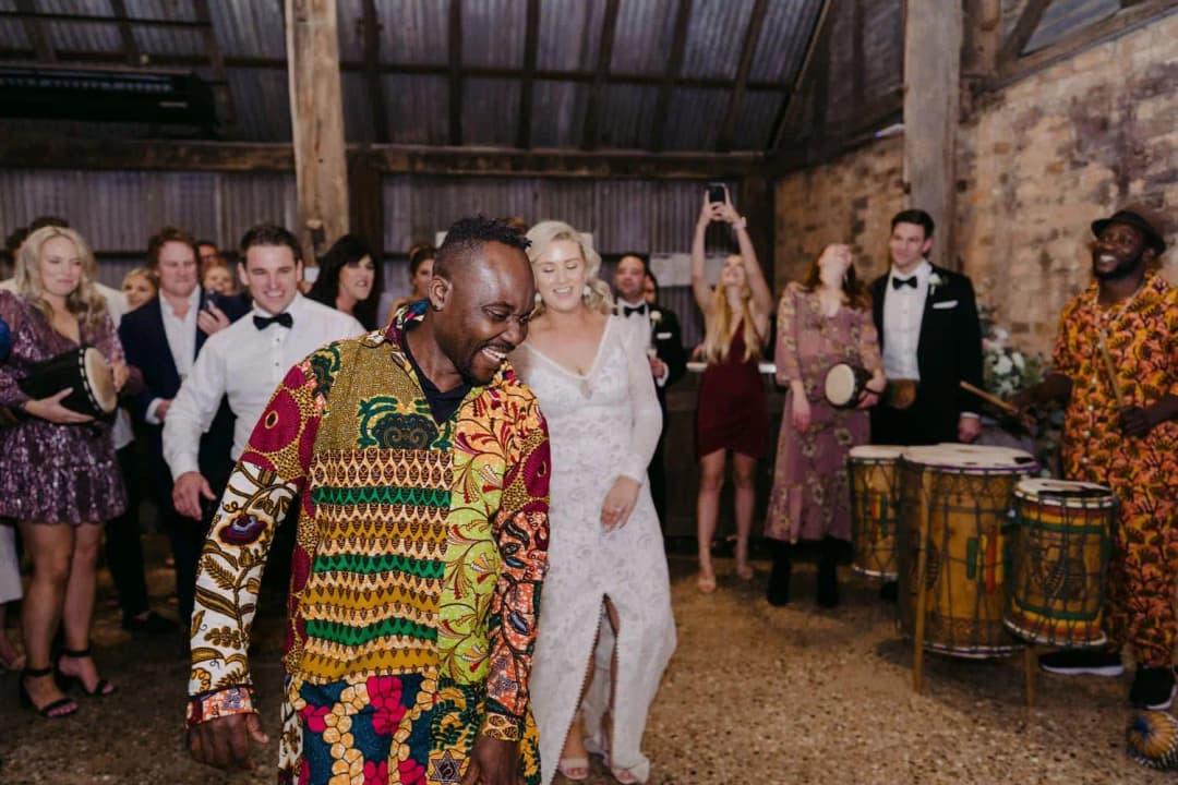 Bride laughing beside a drummer as guests dance behind them.