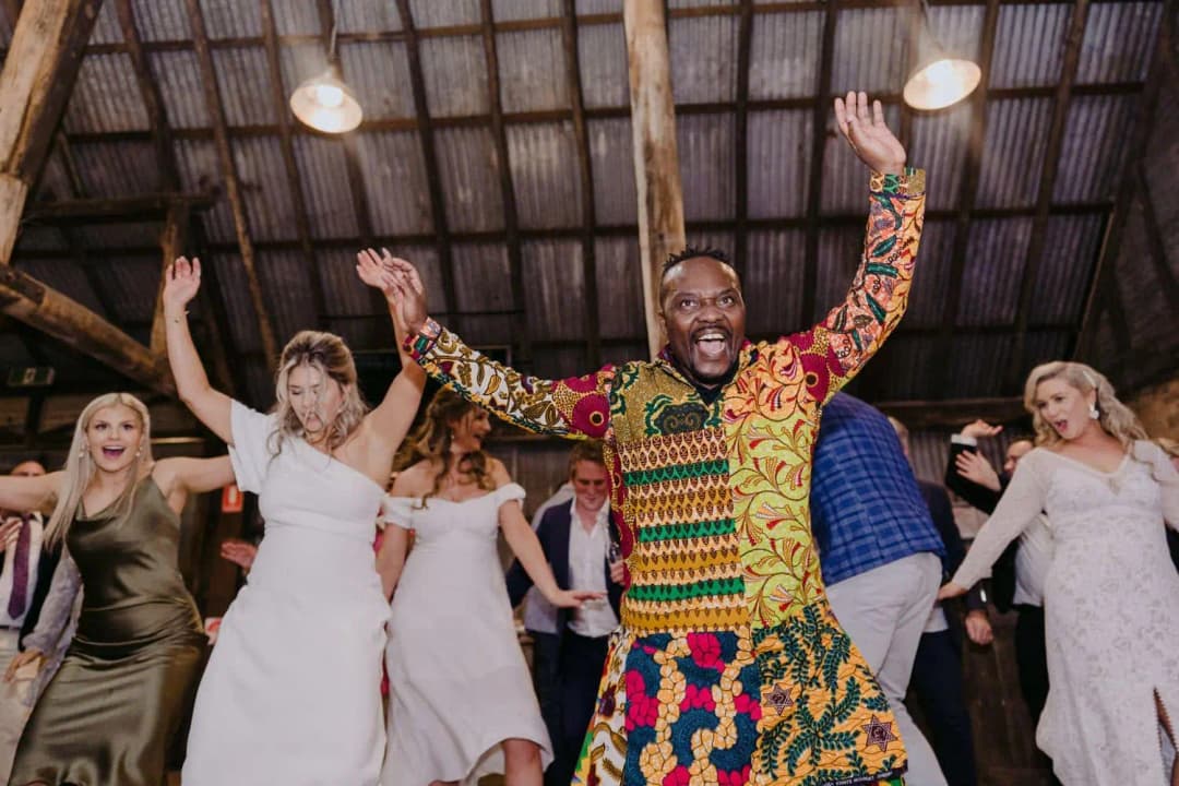 Drummer raising both arms as the bride and guests dance beside him.